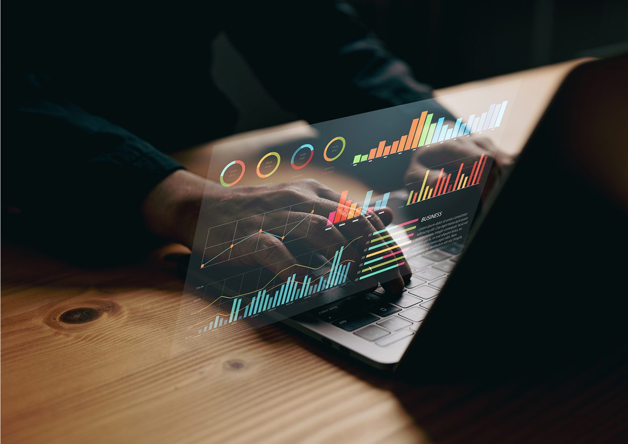 Hands typing on laptop with data graphs.
